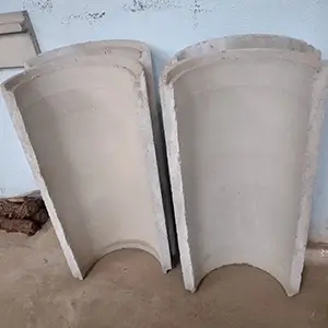 imagem com calhas curvas de concreto enfileiradas e apoiadas em uma parede azul, sobre um piso de terra
