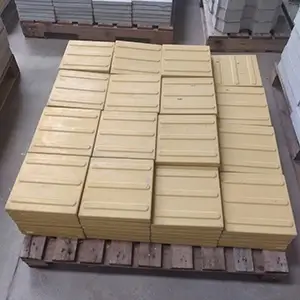 imagem com peças de piso tátil caramelo empilhadas sobre um pallet, dentro de um galpão
