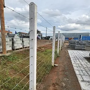 postes retos com grade de arames instalados ao redor de um terreno com grama, cercando-o